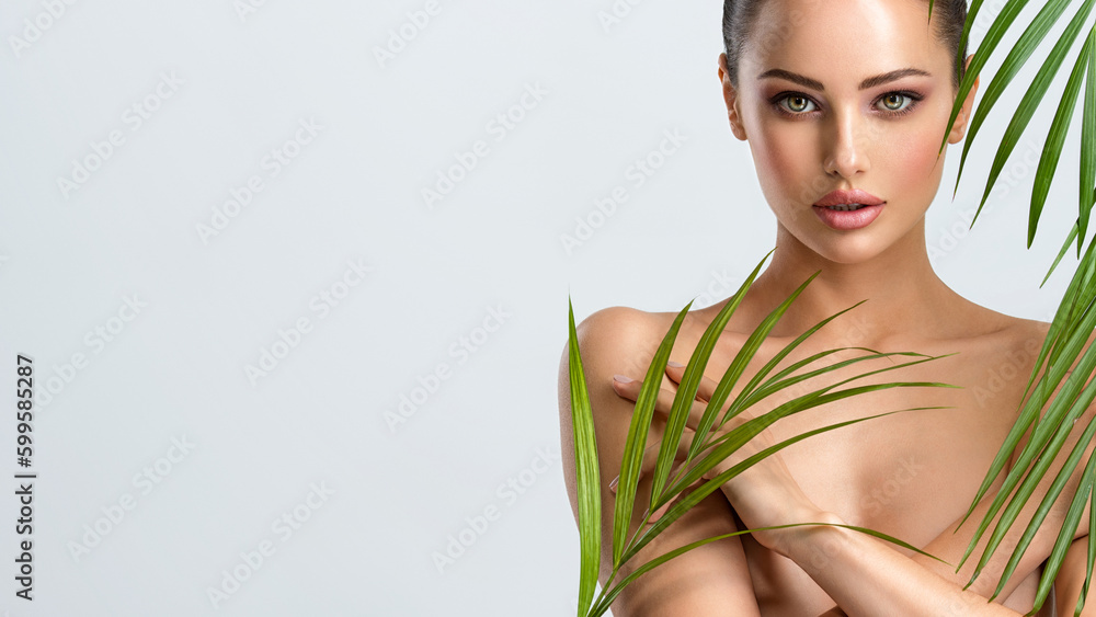 Young beautiful woman with healthy skin of body and palm leaves. Tanned body of an attractive white girl with green plants. Woman hiding her naked body with hands. Young beautiful woman with healthy skin of body and palm leaves. Tanned body of an attractive white girl with green plants. Woman hiding her naked body with hands.