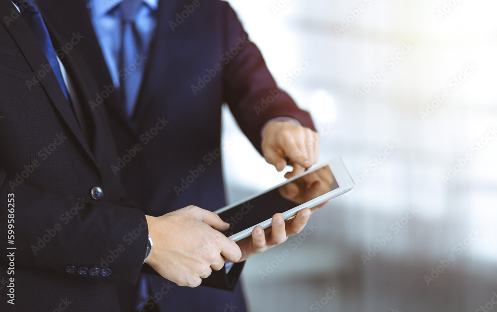 Business people use a tablet computer for discussion of their new project, standing in a sunny modern office. Unknown businessman or male entrepreneur with a colleague at workplace Business people use a tablet computer for discussion of their new project, standing in a sunny modern office. Unknown businessman or male entrepreneur with a colleague at workplace