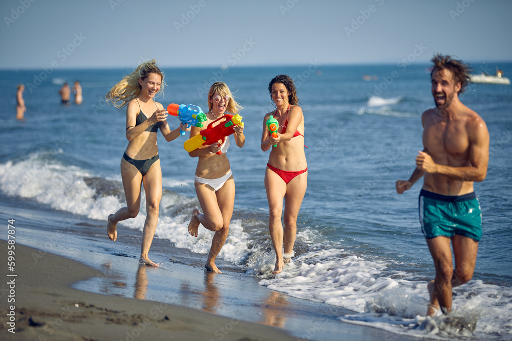 Group of friends playing with water guns at beach together. Young adults on summer vacation. Holiday, fun, travel, lifestyle concept. Group of friends playing with water guns at beach together. Young adults on summer vacation. Holiday, fun, travel, lifestyle concept.