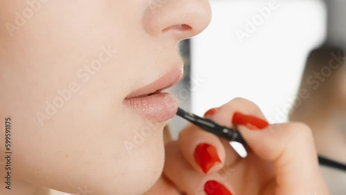 Glamorous makeup gracefully emphasizes the physiognomy of the model, making her face an unsurpassed masterpiece. Summing up woman's lips with brush in a beauty salon with a makeup artist. Red manicure photo