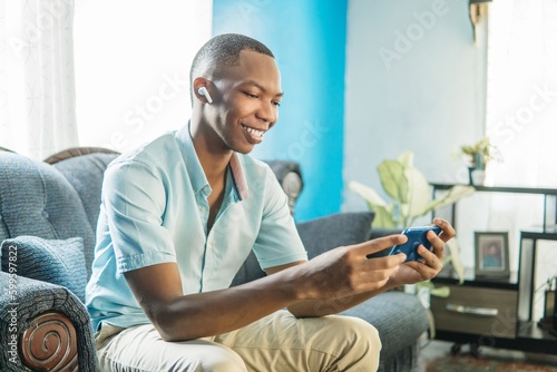 Young black man with earphones watching a movie on the phone.