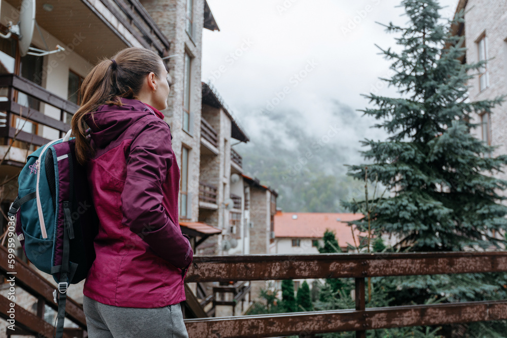 A young woman stands and looks at the mountains in the rain. Tourist in a mountain village