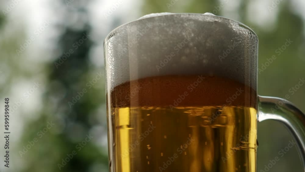 Alcohol beverage with yellow color, air bubble and beautiful green nature background. Close up of foam beer in glass after pour from bottle at outdoors. Look fresh and cool for drink. Slow motion Alcohol beverage with yellow color, air bubble and beautiful green nature background. Close up of foam beer in glass after pour from bottle at outdoors. Look fresh and cool for drink. Slow motion