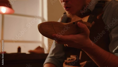 Craftsman grinds wooden shoe last with sandpaper in shoemaker workshop. Handmade shoe making. 
