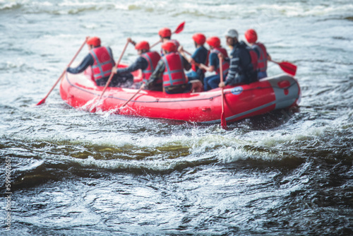 Red raft boat during whitewater rafting extreme water sports on water rapids, group of sportsmen in wetsuits kayaking and canoeing on the river, water sports team with a big splash of water