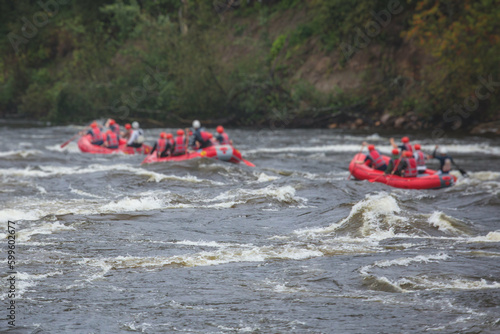 Red raft boat during whitewater rafting extreme water sports on water rapids, group of sportsmen in wetsuits kayaking and canoeing on the river, water sports team with a big splash of water
