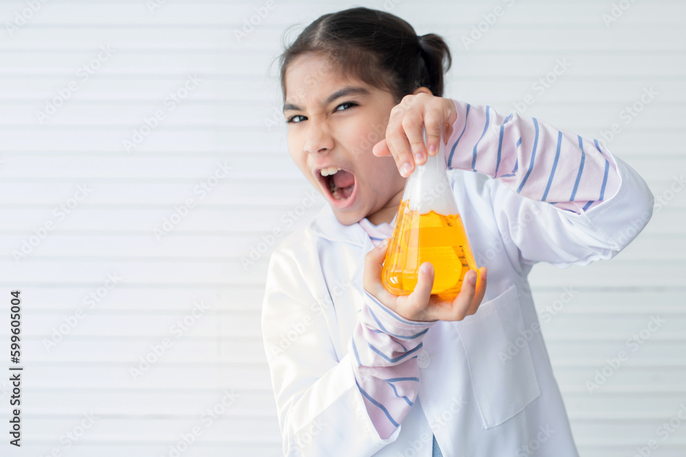 Cheerful Asian school girl wearing lab coat showing yellow liquid in beaker on white wall, learning chemistry in laboratory at school Cheerful Asian school girl wearing lab coat showing yellow liquid in beaker on white wall, learning chemistry in laboratory at school