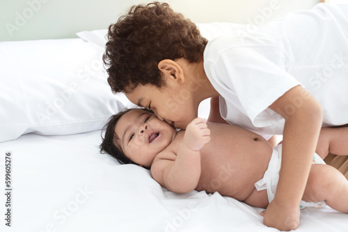Happy boy loves and kissing of newborn baby sister on bed at home, Family love