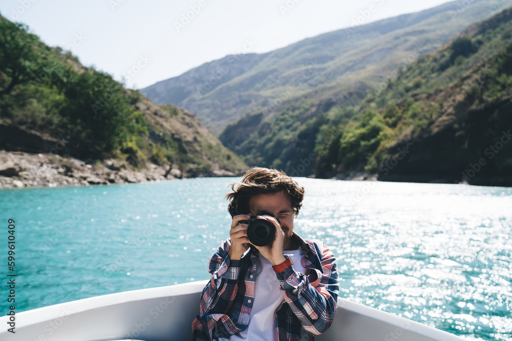 Traveling man sitting in boat and taking photo on camera