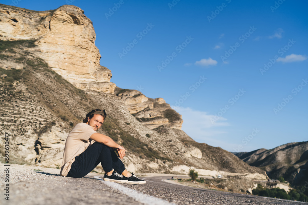 Naklejka premium Young man sitting on asphalt road in sunlight