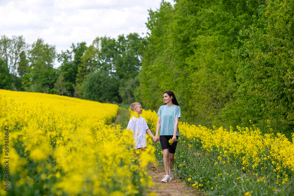 Mom and son are running through the field with rapeseed. Yellow field