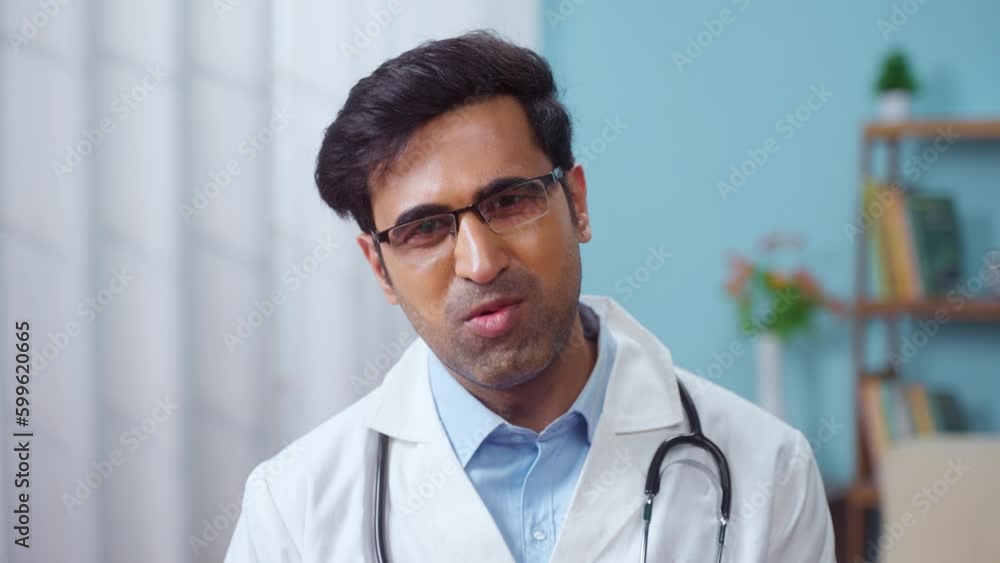 Confident indian doctor talking on video call by looking at camera from hospital with patients - concept of online counseling, medical advice and consultation Confident indian doctor talking on video call by looking at camera from hospital with patients - concept of online counseling, medical advice and consultation