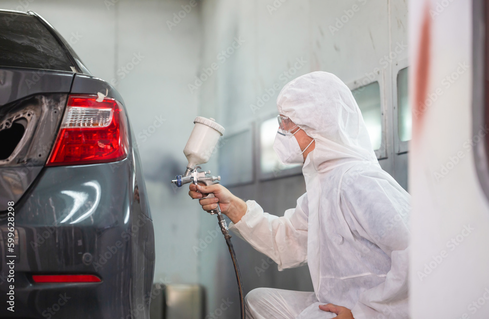 Mechanic painting car in chamber. Worker using spray gun and airbrush