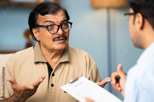 Indian banker taking sign from senior woman by giving money at home - concept of financial helping, investment and retirement pension