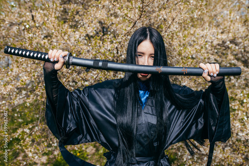 Young asian girl in traditional black kimono with katana against nature background