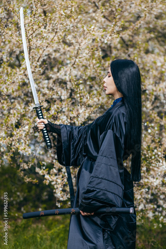 Young asian girl in traditional black kimono with katana against nature background