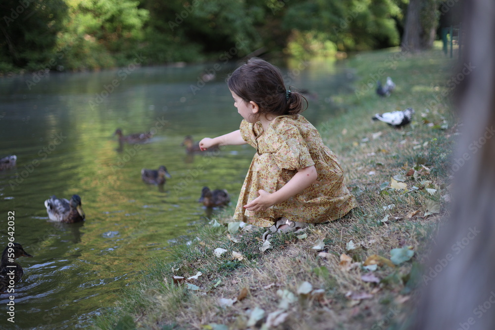 Fototapeta premium Little baby girl feeds ducks in park near the lake 