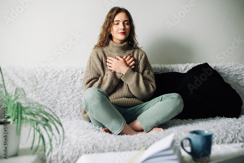 Fotografia Relaxation techniques: Woman practicing pranayama in lotus position on bed, brea