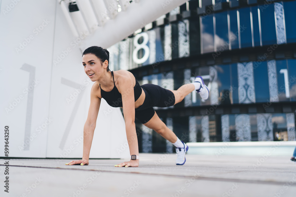 Fototapeta premium Positive sportswoman training on street in city district