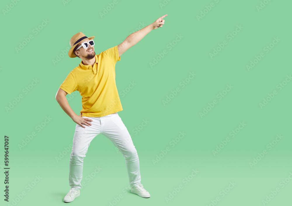 Funny young trendy man in hat and sunglasses isolated on green studio background have fun dancing. Overjoyed guy point at good sale deal or offer. Entertainment and hobby. Advertising. Funny young trendy man in hat and sunglasses isolated on green studio background have fun dancing. Overjoyed guy point at good sale deal or offer. Entertainment and hobby. Advertising.