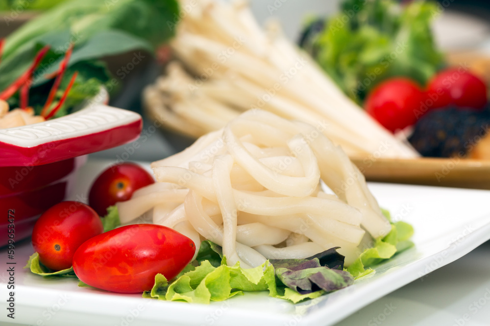 Close up of white pho big noodle on dish with red tomato and various vegetable in background Close up of white pho big noodle on dish with red tomato and various vegetable in background