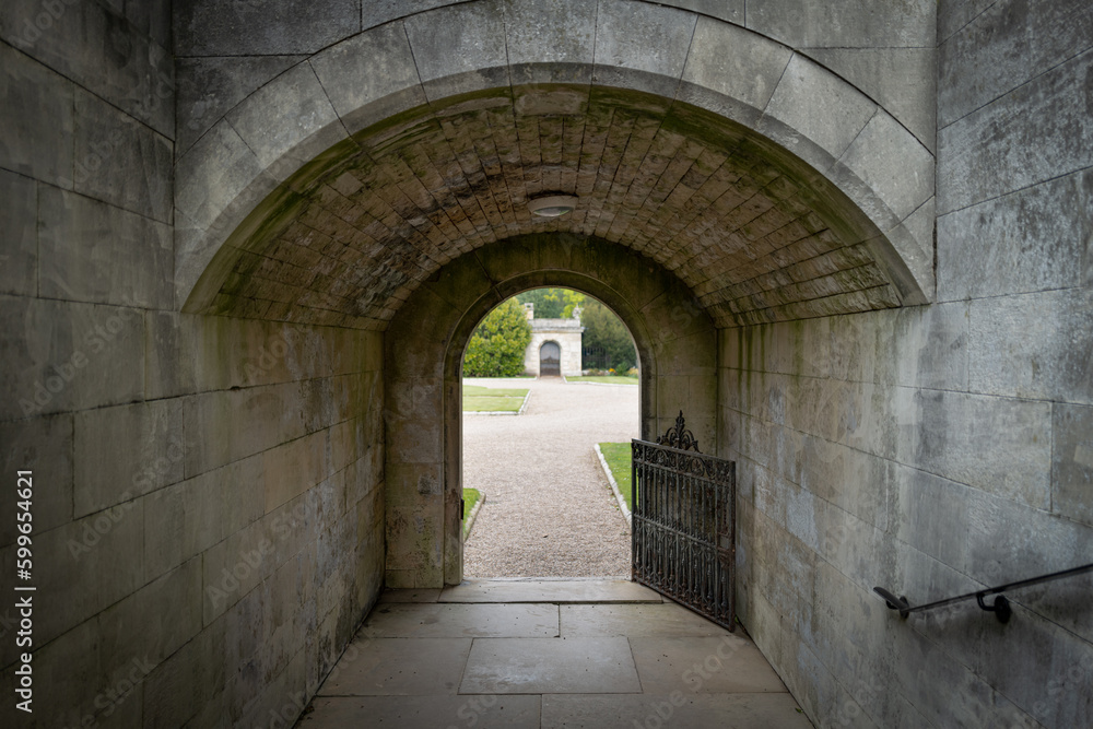 Opened gated entrance to a stately home garden. The stone tunnel travels under a rear level of a grand house.
