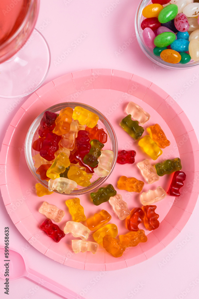 Plate with gummy bears, jelly beans and a glass with a pink drink on a pink table. Coloring in food. Parties and celebrations Plate with gummy bears, jelly beans and a glass with a pink drink on a pink table. Coloring in food. Parties and celebrations