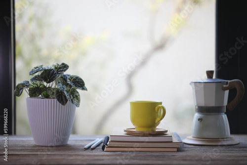 Print op canvas Yellow coffee cup and moka pot and plant pot in front of glass window