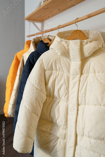 Winter clothes on a hanger in the room. A row of down jackets hang on a white background.