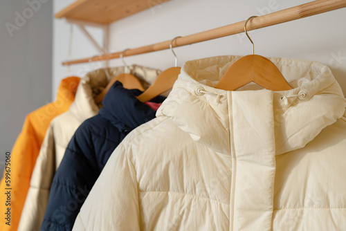 Winter clothes on a hanger in the room. A row of down jackets hang on a white background.