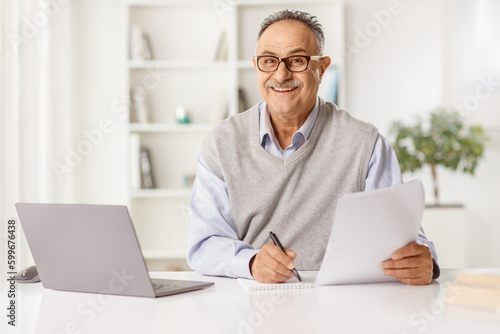Mature man sitting in front of a laptop computer at home and writing a paper document