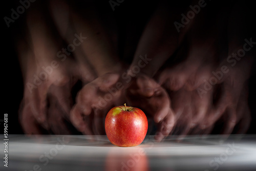 Chciwe ręce pożądają jabłka leżącego na stole. Kuszenie