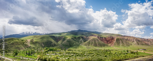 This aerial photo displays a vast valley encompassed by gentle hills and high mountains under a cloudy sky