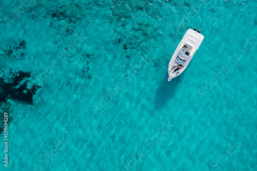 A yacht floating on the beautiful blue waters of Formentera, with a couple lying down and resting on board. © Sobresalto