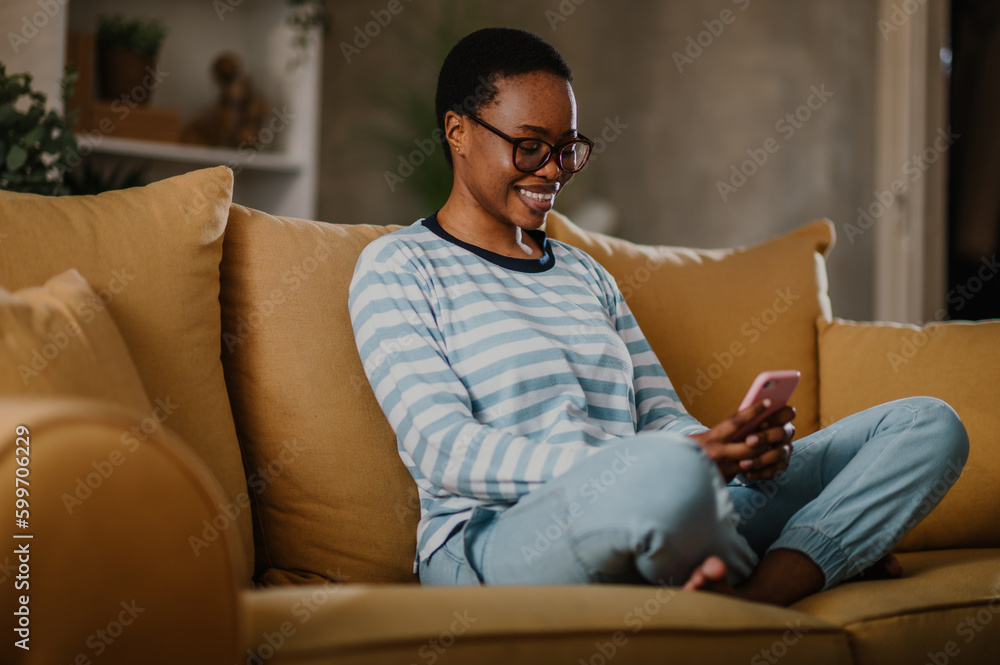 African american woman using a smartphone while sitting on a yellow sofa at home