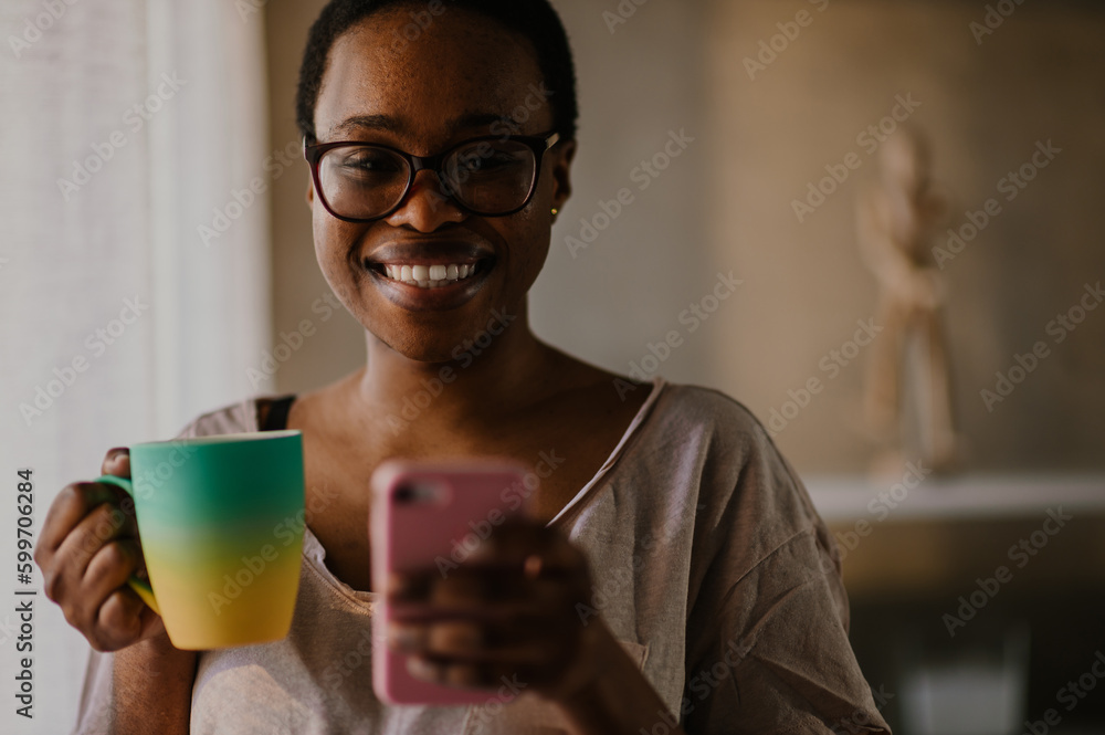 African american woman using smartphone while drinking coffee at home