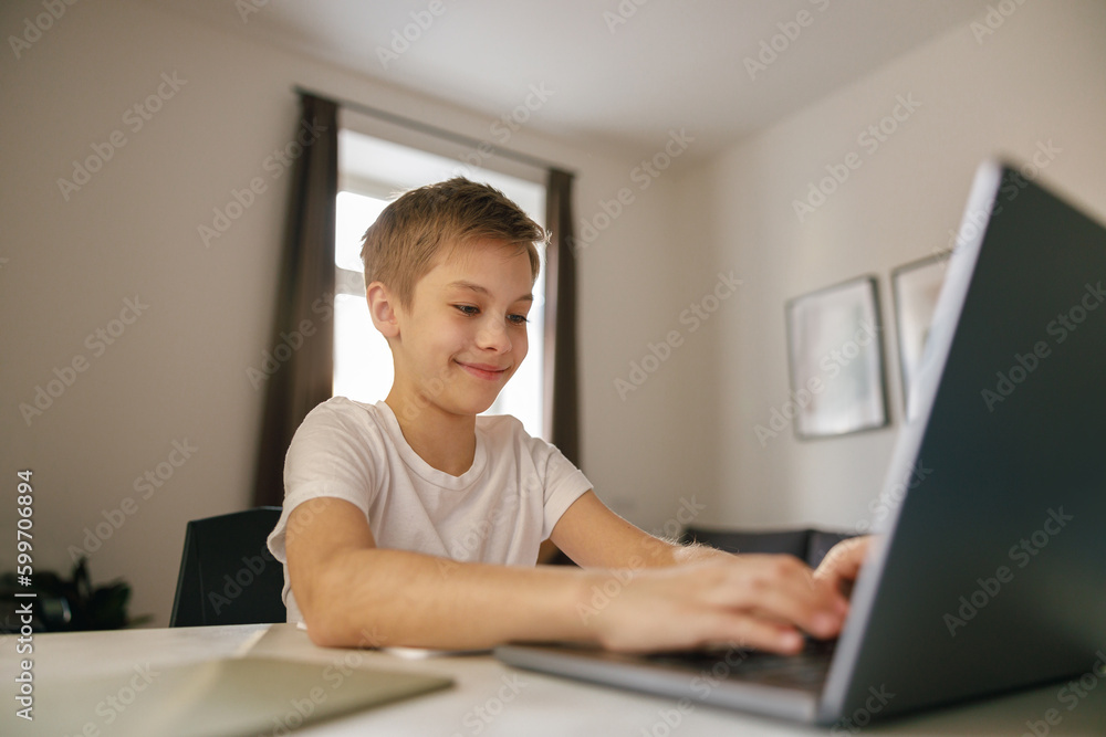 Small happy boy having online video lesson at laptop sitting at the table in his room. E-learning Small happy boy having online video lesson at laptop sitting at the table in his room. E-learning