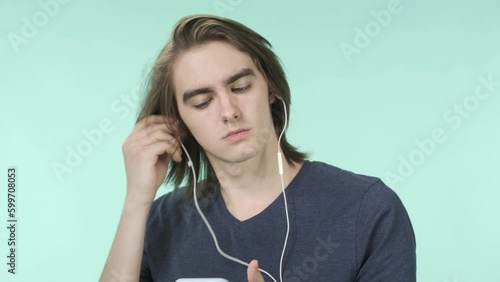 A handsome young man puts on wired headphones and holds a phone in his hand