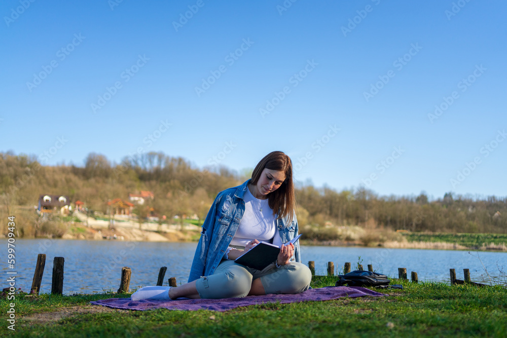 Woman at lakeside writing in a notebook. Nature concept. Self reflection. Woman at lakeside writing in a notebook. Nature concept. Self reflection.