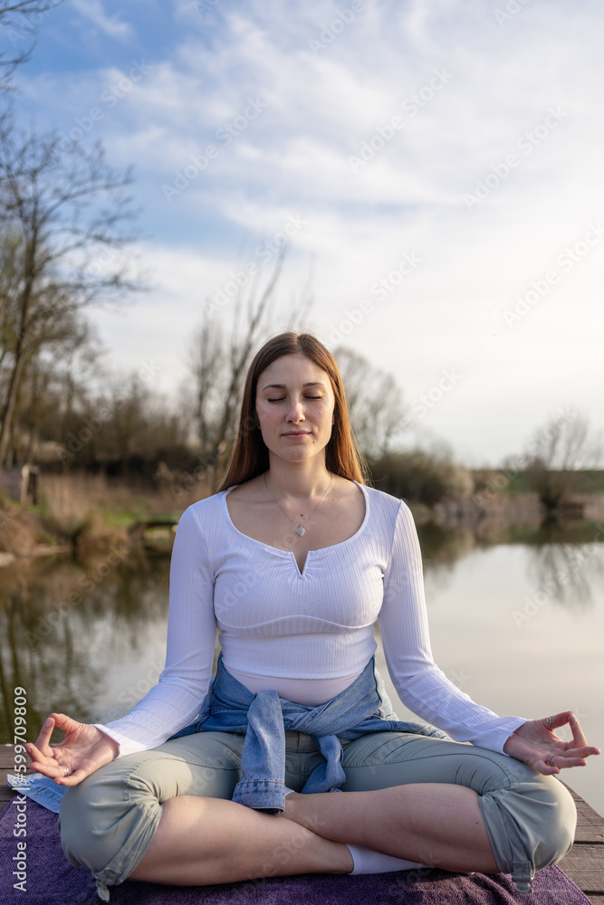 Woman relaxingly practicing meditation in nature by the lake. Nature background. Spiritual and emotional concept.