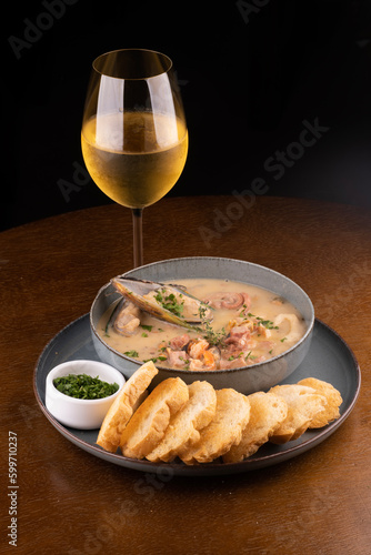 Seafood soup with toasted New Zealand mussels and green onions on wooden table. Portrait with glass of white wine.