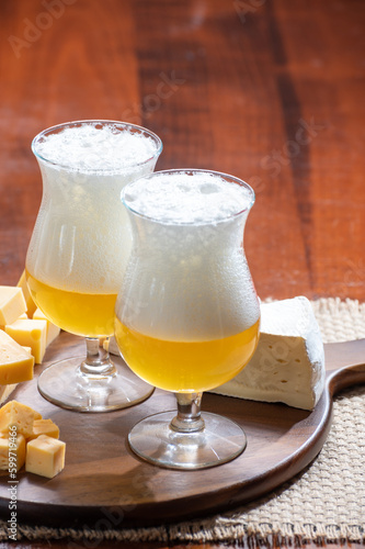 Glasses of Belgian light blonde beer made in abbey and wooden board with variety of belgian cheeses photo