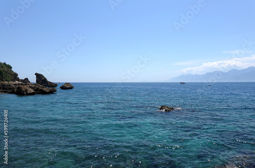 Beautiful calm sea and rocks in front and high mountains in haze at far in sunny summer day