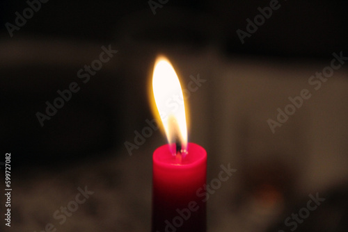 Gentle light from a burning red candle on a blurred background