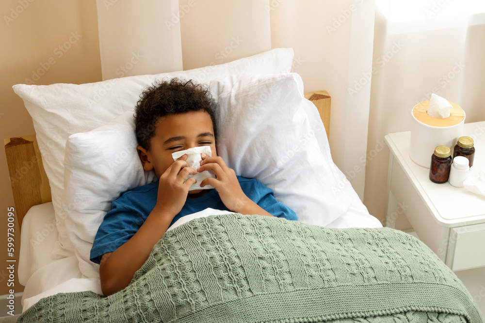 African-American boy with scarf and tissue blowing nose in bed indoors, above view. Cold symptoms African-American boy with scarf and tissue blowing nose in bed indoors, above view. Cold symptoms