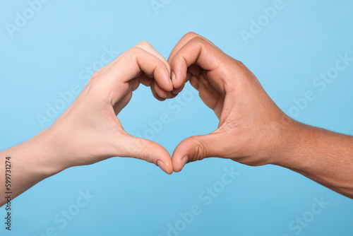 International relationships. People making heart with hands on light blue background, closeup