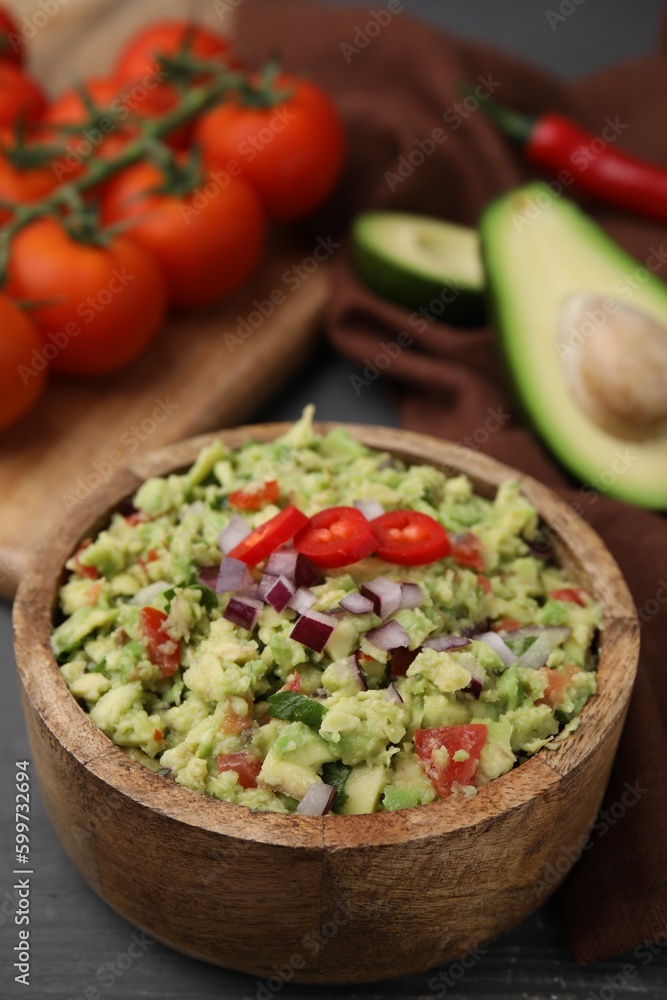 Bowl of delicious guacamole and ingredients on grey wooden table, closeup