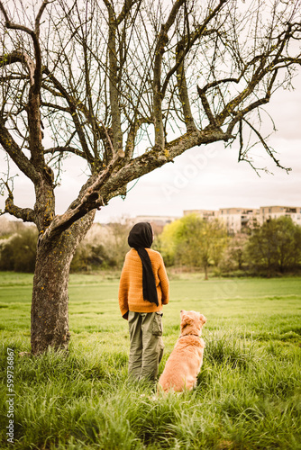 muslim girl standing peaceful with a dog, two best friends under a tree in a park while watching the view on a walk photo