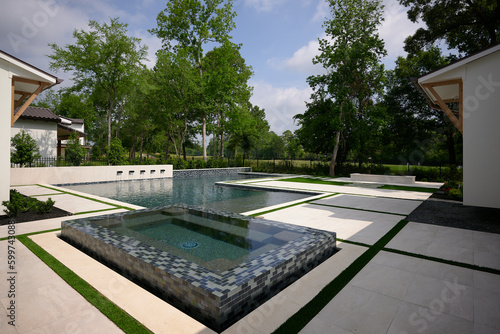 THE WOODLANDS, TEXAS - MAY 5th 2023: an outdoor pool and spa with water features on a hot sunny day. The blue water is sparkling and the Mediterranean style house is white with a terracotta roof.