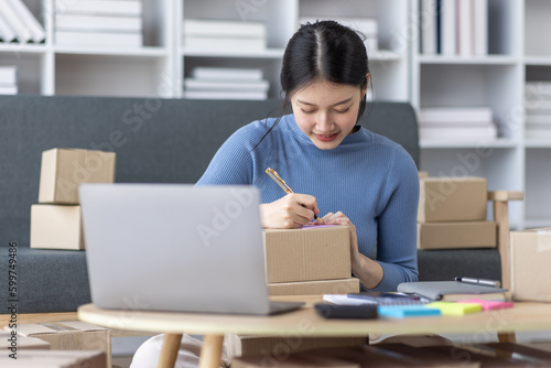 Asian business woman on sofa using a laptop computer checking customer order online shipping boxes at home. Starting SME Small business entrepreneur freelance. Online business, SME Work home concept. 